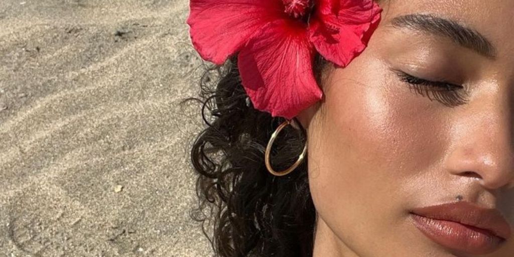 Close-up of a woman lying on sand with a red hibiscus flower in her curly hair.