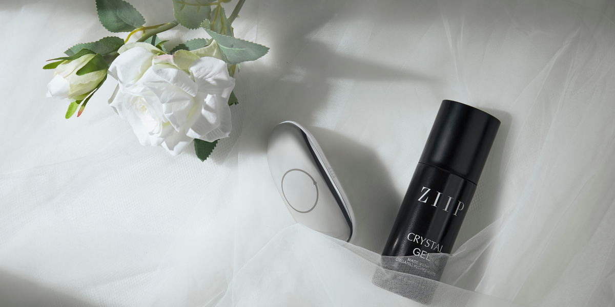 ZIIP GX and a ZIIP gel bottle resting on white bedding, next to white flowers.