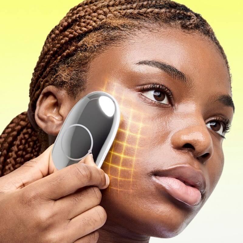 A close-up of a woman holding a ZIIP HALO against her cheek, with a glowing yellow grid graphic overlaid on her skin. The background is a soft yellow gradient.